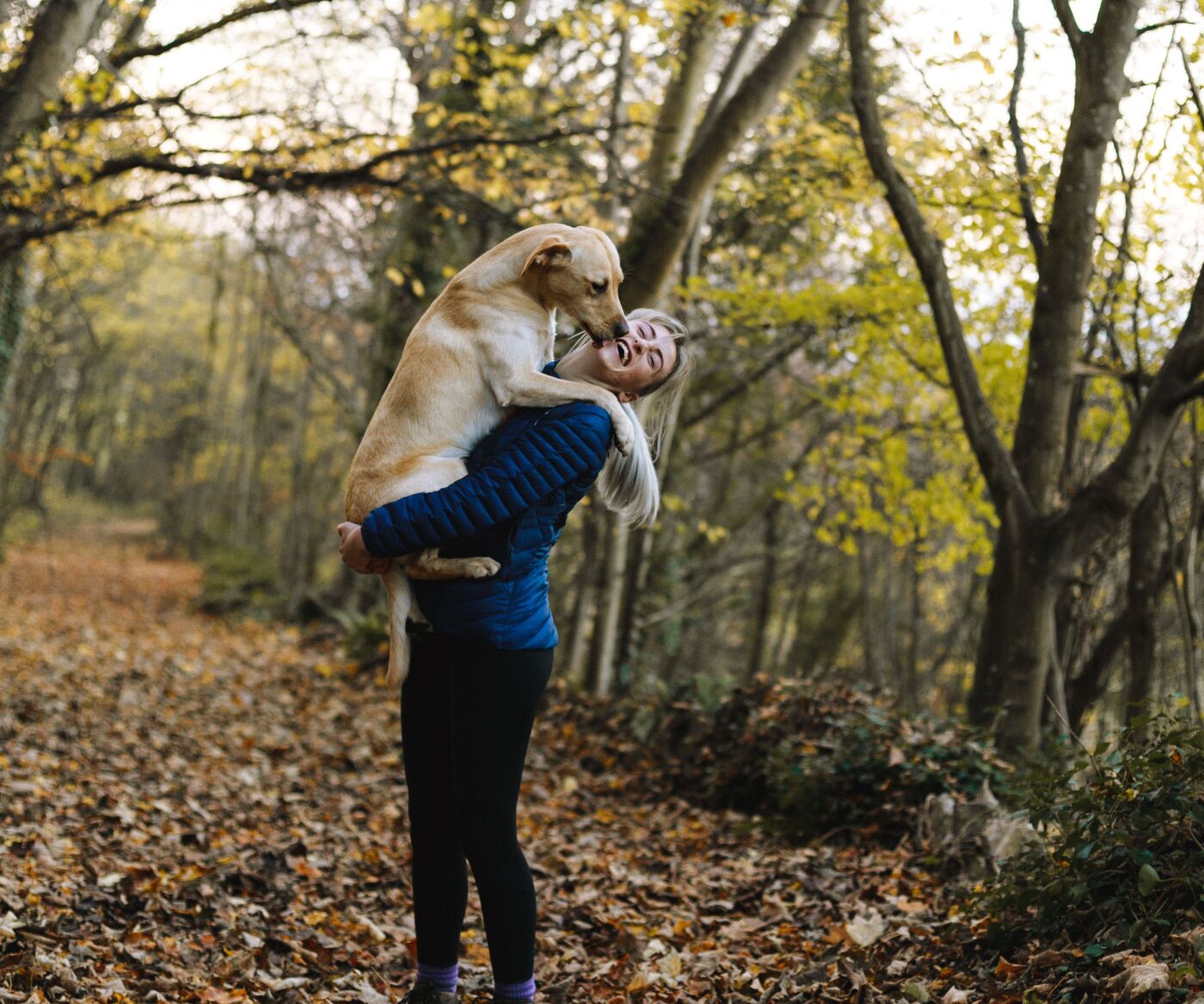 A woman laughing as her dog hugs her on an autumn forest walk