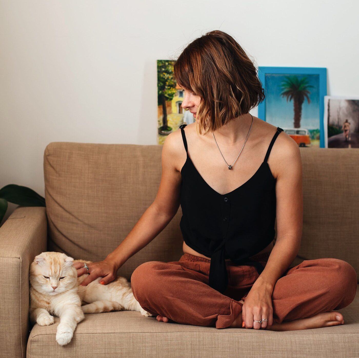 A woman on the sofa reaching over to stroke her cream cat sitting beside her