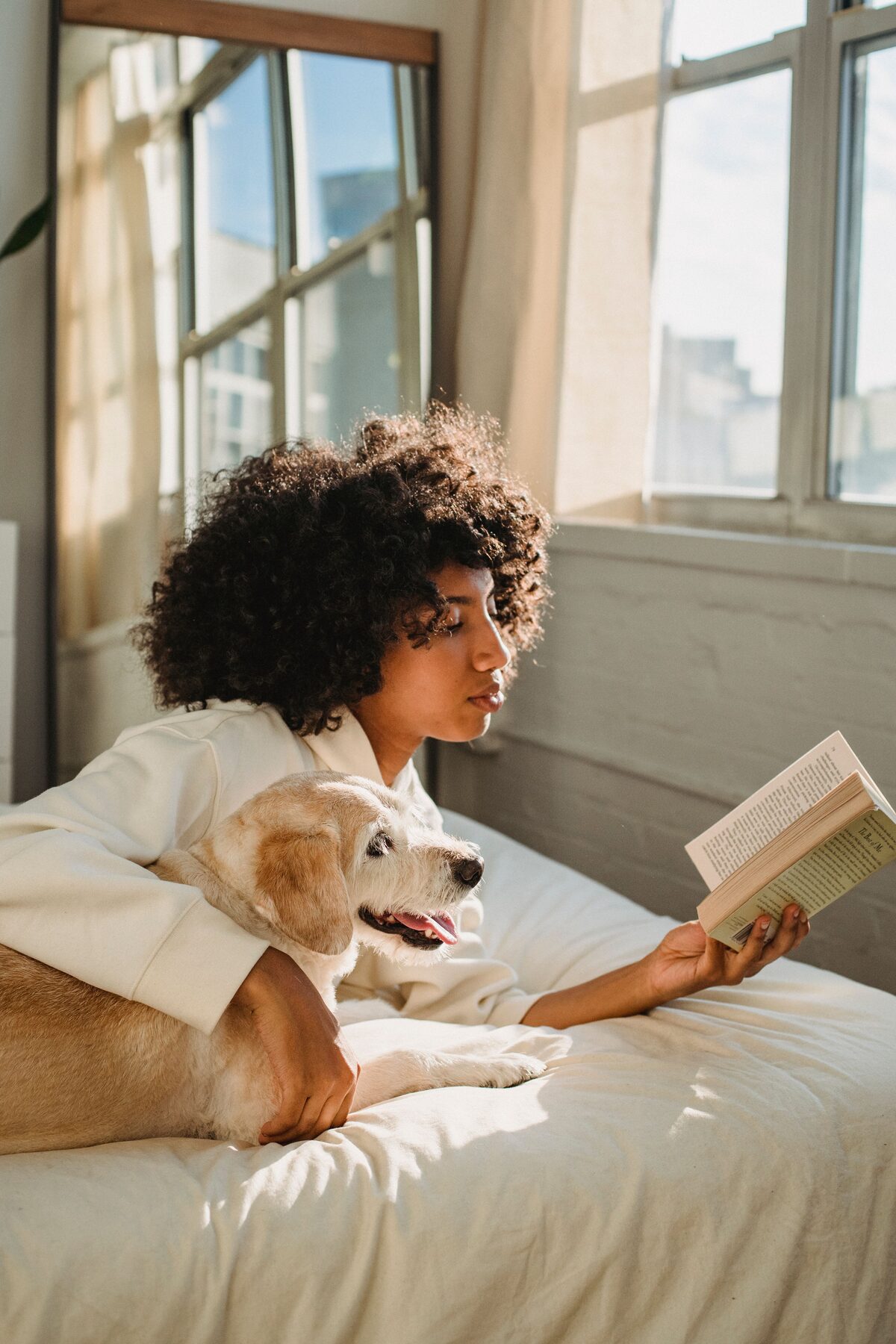A quiet morning: a woman reads in bed while her dog rests beside her