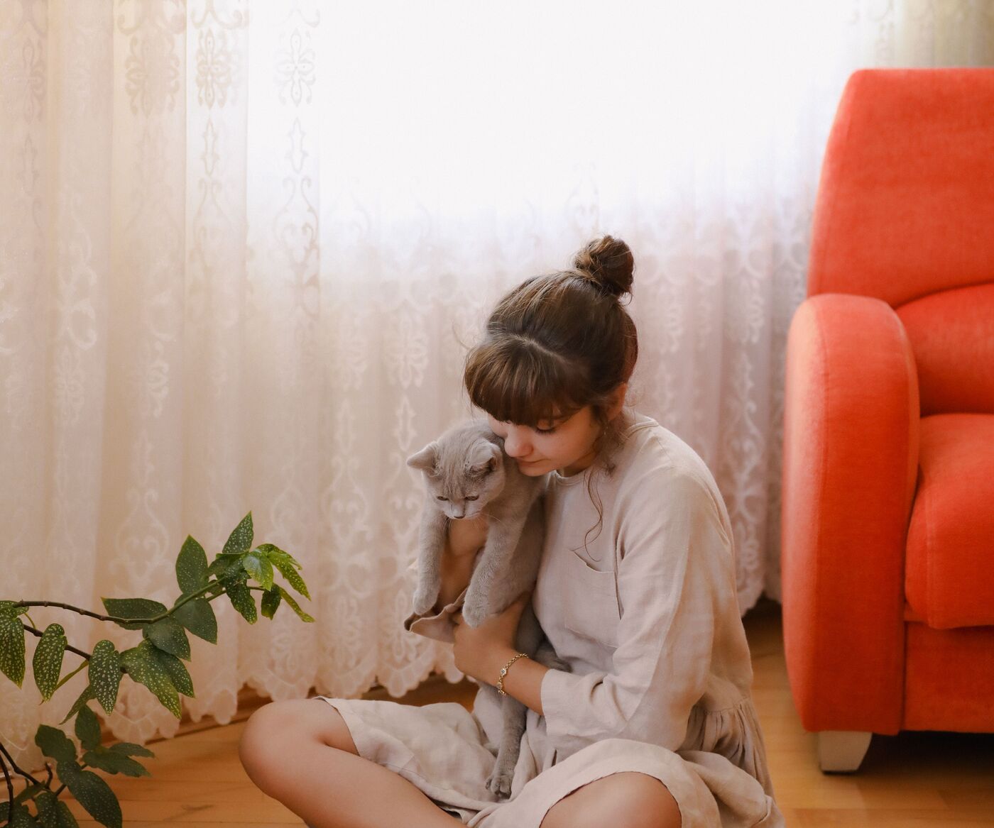 A young woman sitting on the floor by the window, quietly holding her grey cat
